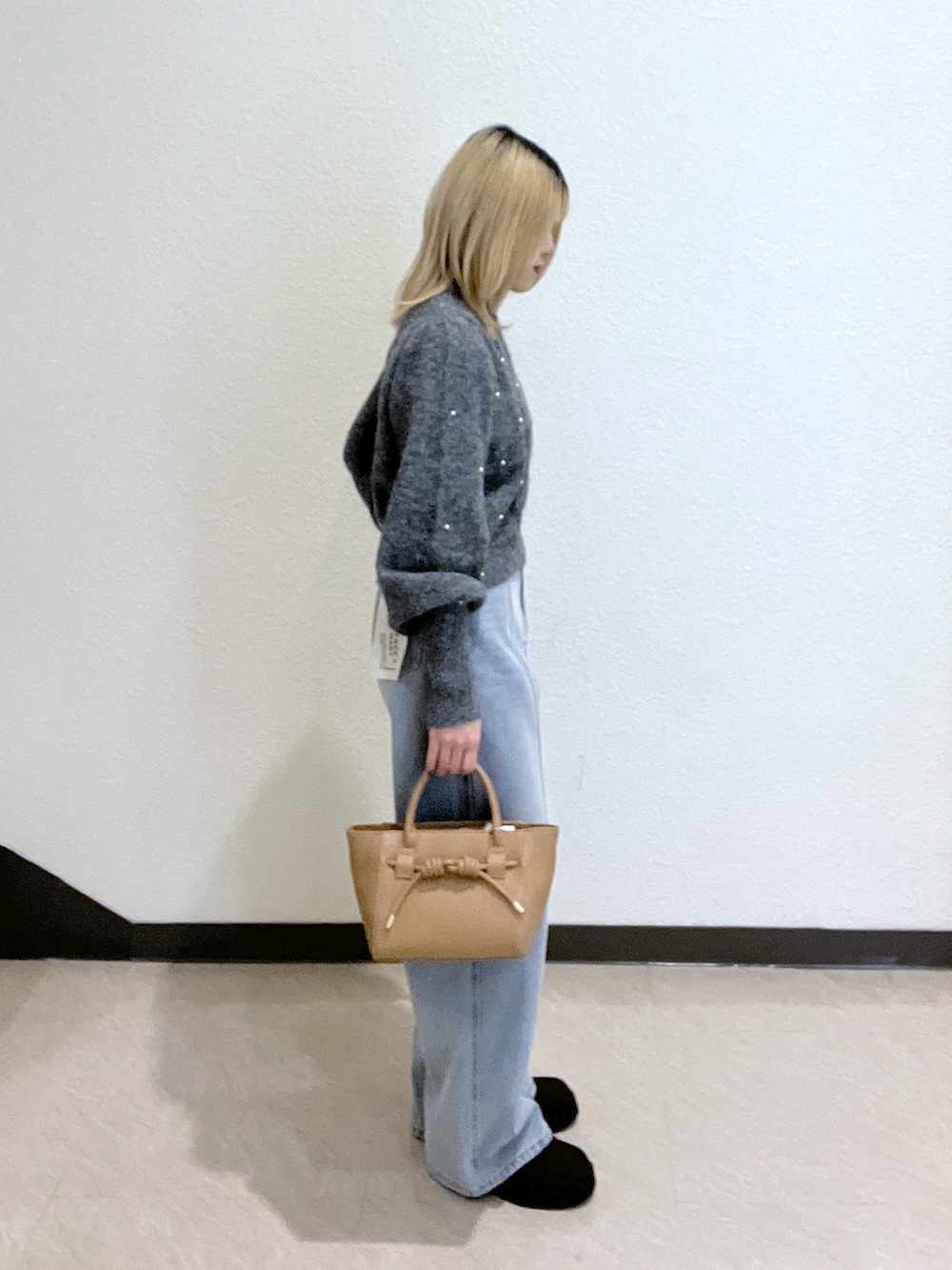 グレー系のニット/セーター、ブルー系のデニムパンツ、ベージュ系のトートバッグを着用したレディースの秋コーディネートの2枚目の写真