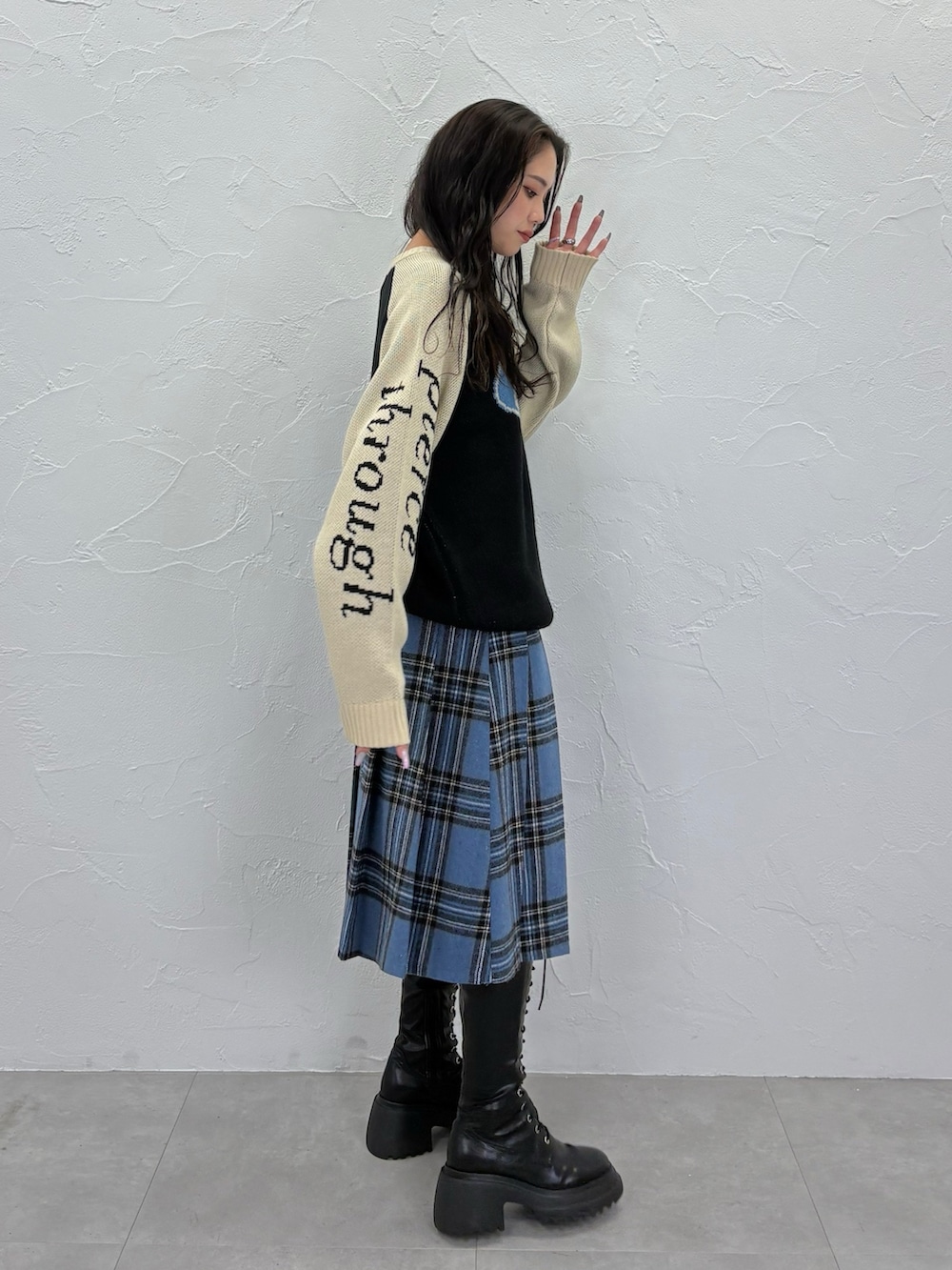 ブラック系のニット/セーター、ブルー系のスカート、ブラック系のブーツを着用したレディースの秋コーディネートの2枚目の写真