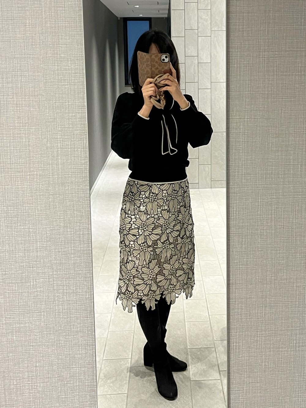 グレー系のスカート、ブラック系のニット/セーター、ブラック系のブーツを着用したレディースの春コーディネートの2枚目の写真