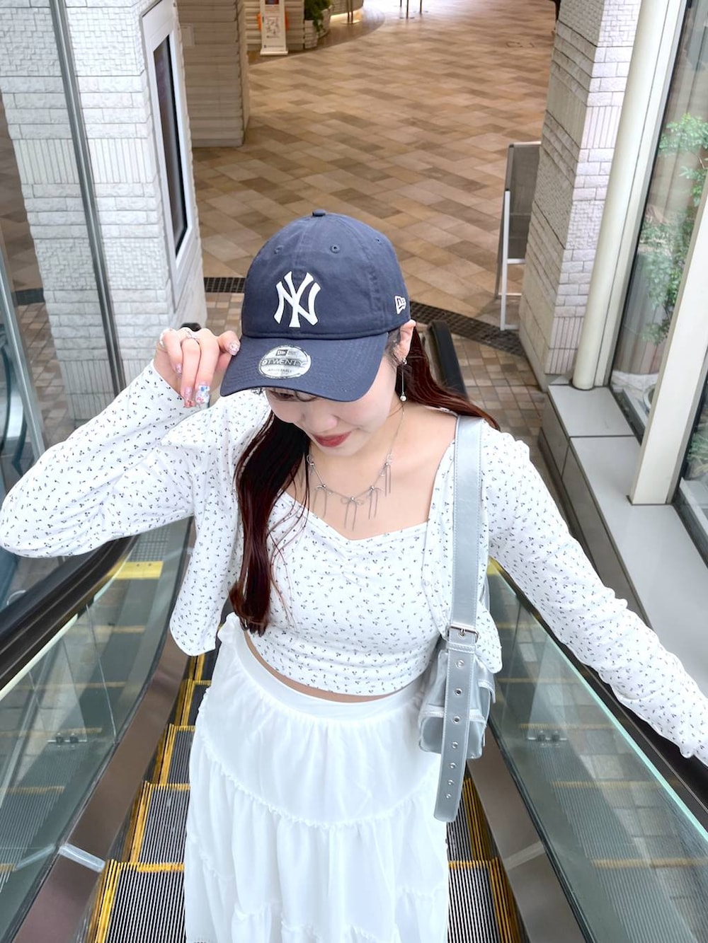 シルバー系のショルダーバッグ、ホワイト系のスカート、ホワイト系のアンサンブルを着用したレディースの春コーディネートの2枚目の写真