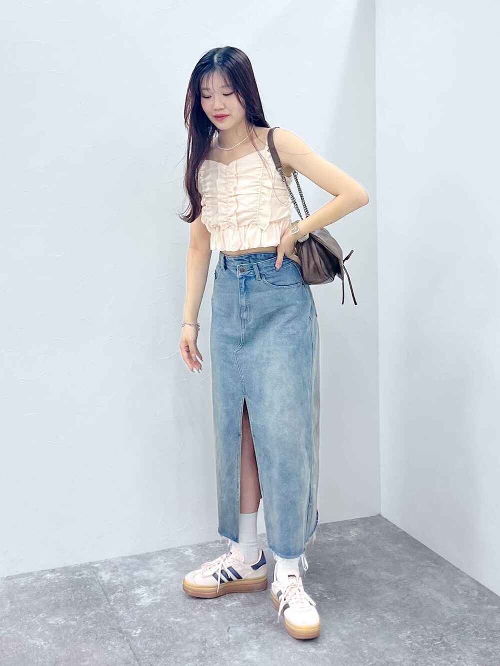 ブラウン系のショルダーバッグ、ホワイト系のキャミソール、ブルー系のデニムスカートを着用したレディースの夏コーディネートの2枚目の写真