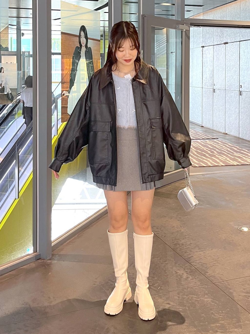 グレー系のスカート、ホワイト系のブーツ、ブラック系のブルゾンを着用したレディースの秋コーディネートの2枚目の写真