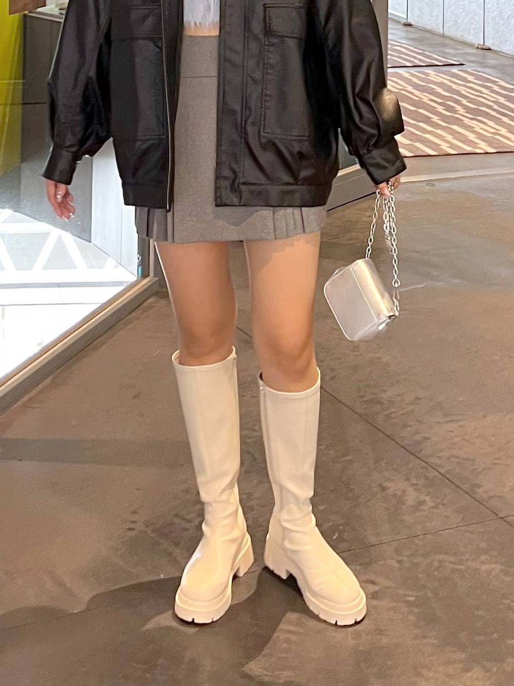 グレー系のスカート、ホワイト系のブーツ、ブラック系のブルゾンを着用したレディースの秋コーディネートの5枚目の写真