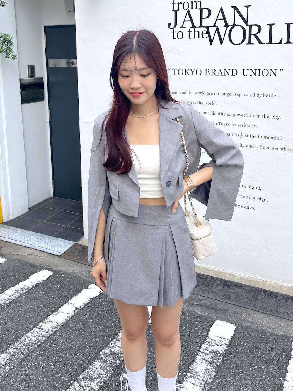 グレー系のテーラードジャケット、ホワイト系のショルダーバッグ、ホワイト系のキャミソールを着用したレディースの夏コーディネートの2枚目の写真