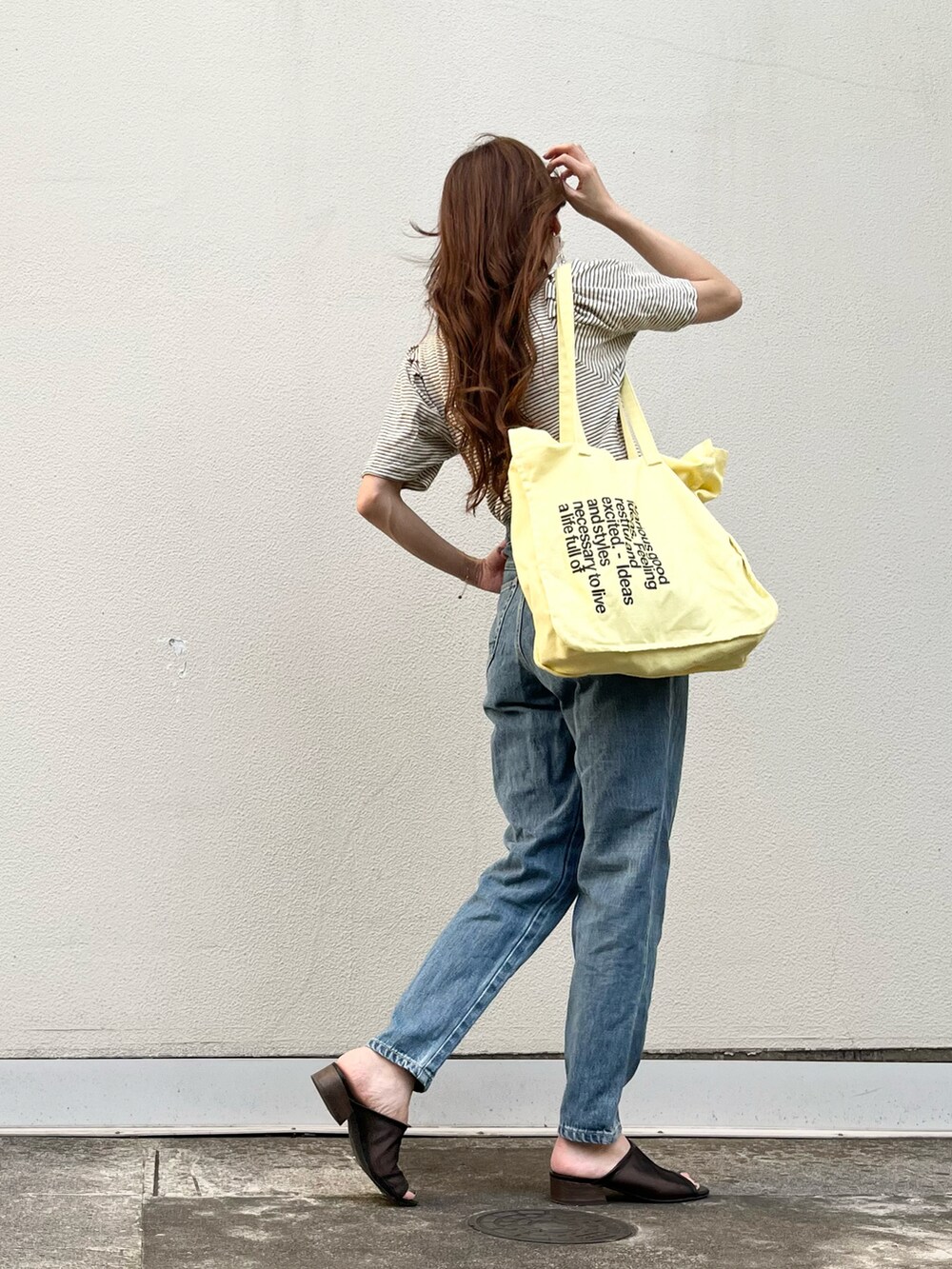 ブルー系のデニムパンツ、イエロー系のトートバッグ、ホワイト系のニット/セーターを着用したレディースの夏コーディネートの2枚目の写真