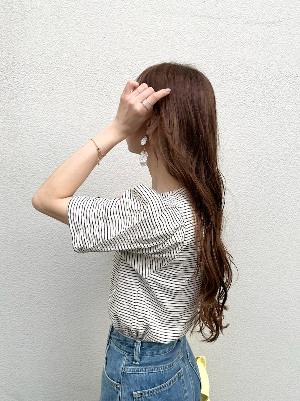 ブルー系のデニムパンツ、イエロー系のトートバッグ、ホワイト系のニット/セーターを着用したレディースの夏コーディネートの4枚目の写真