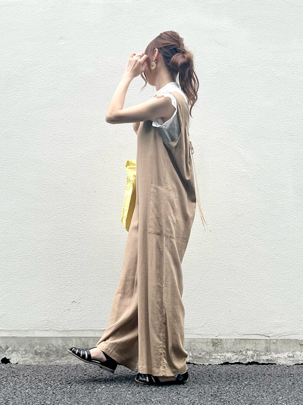 イエロー系のトートバッグ、ベージュ系のサロペット/オーバーオール、ホワイト系のシャツ/ブラウスを着用したレディースの夏コーディネートの3枚目の写真