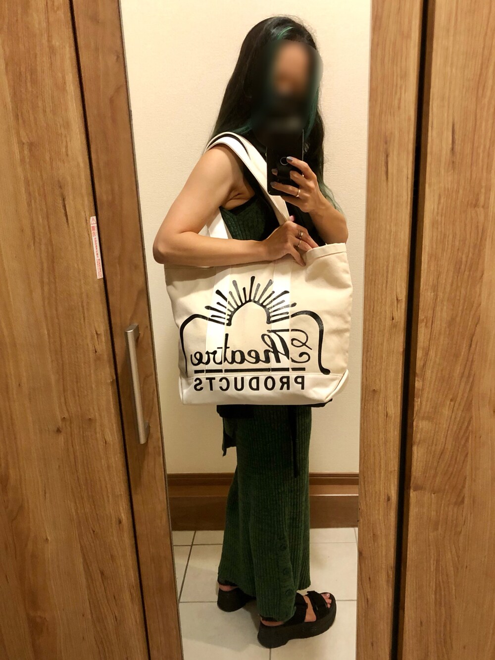 ベージュ系のトートバッグ、ブラック系のベスト、グリーン系のワンピースを着用したレディースの秋コーディネートの3枚目の写真