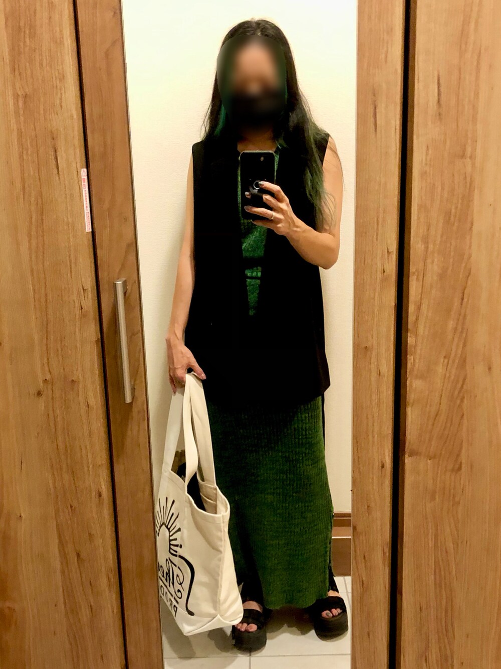 ベージュ系のトートバッグ、ブラック系のベスト、グリーン系のワンピースを着用したレディースの秋コーディネートの2枚目の写真