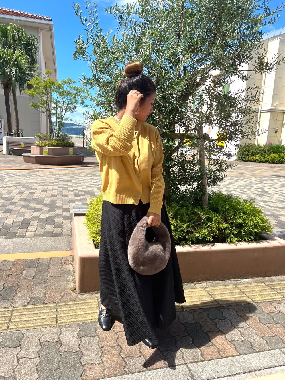 イエロー系のカーディガン/ボレロ、ブラック系のスカート、ブラウン系のハンドバッグを着用したレディースの秋コーディネートの2枚目の写真