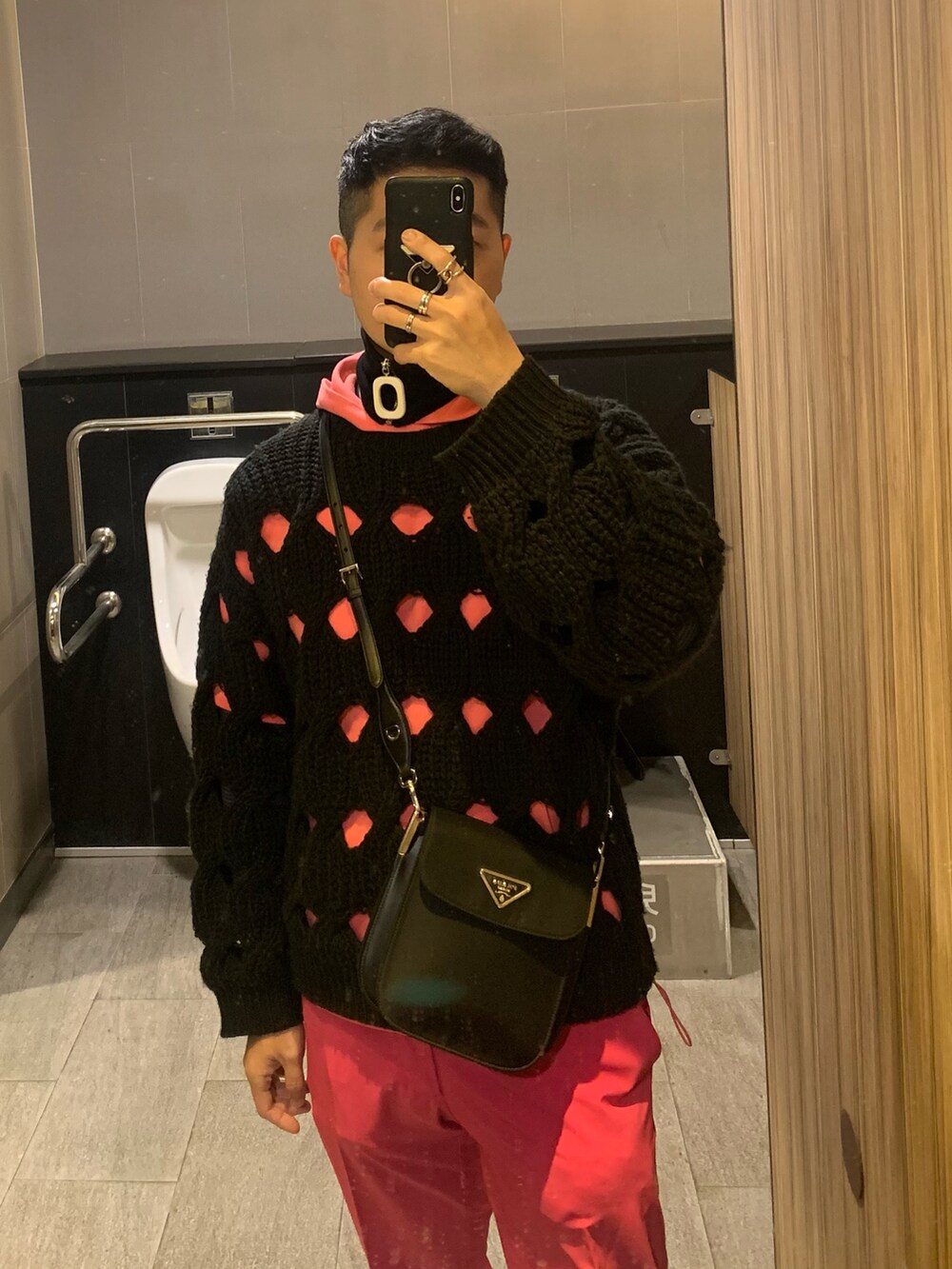 ブラック系のニット/セーター、ブラック系のバッグ、ピンク系のチノパンツを着用したメンズの冬コーディネートの2枚目の写真