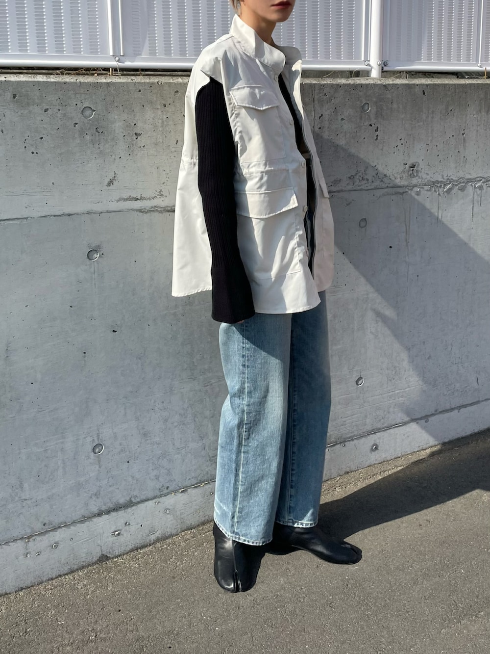 ブルー系のデニムパンツ、ホワイト系のベスト、ブラック系のニット/セーターを着用したレディースの春コーディネートの2枚目の写真