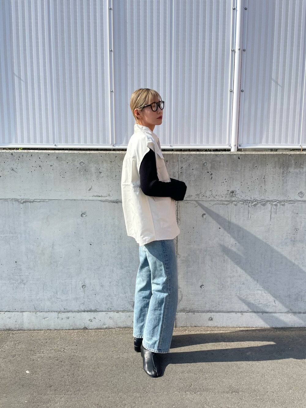 ブルー系のデニムパンツ、ホワイト系のベスト、ブラック系のニット/セーターを着用したレディースの春コーディネートの3枚目の写真