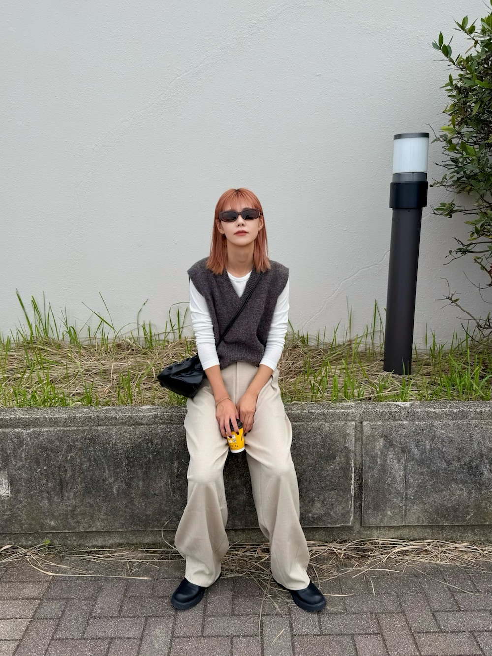 ブラウン系のベスト、ホワイト系のスラックス、ブラック系のサンダルを着用したレディースの秋コーディネートの2枚目の写真