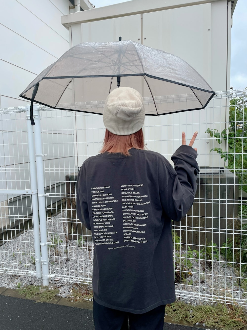 ブラック系のTシャツ/カットソー、ブラック系のサンダル、ブラウン系の長傘を着用したレディースの秋コーディネートの2枚目の写真