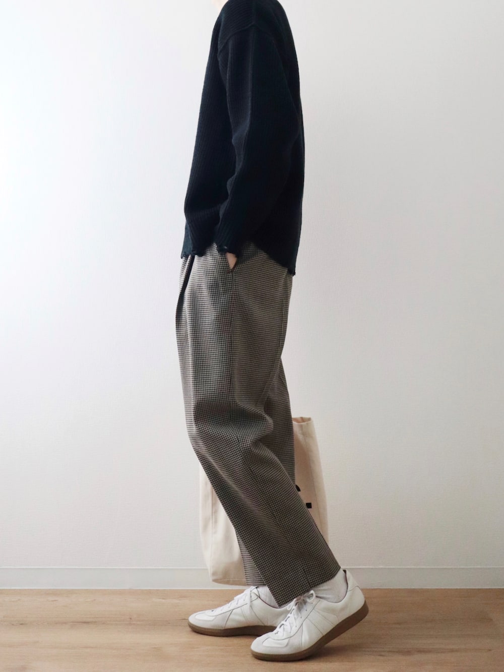 ブラック系のニット/セーター、ベージュ系のスラックス、ホワイト系のスニーカーを着用したメンズの秋コーディネートの2枚目の写真