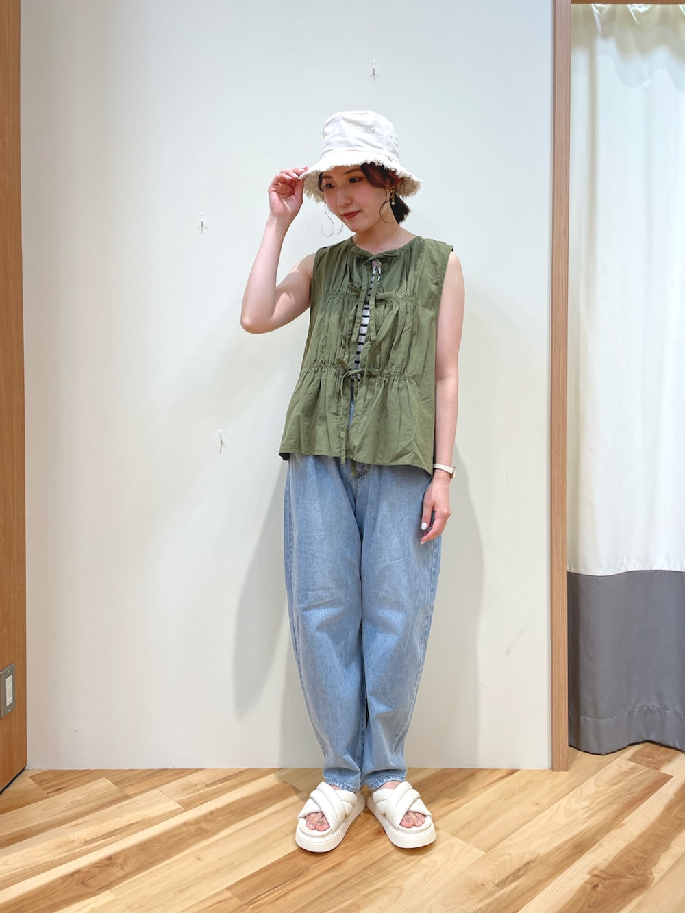 ブルー系のデニムパンツ、ホワイト系のサンダル、グリーン系のベストを着用したレディースの春コーディネートの2枚目の写真