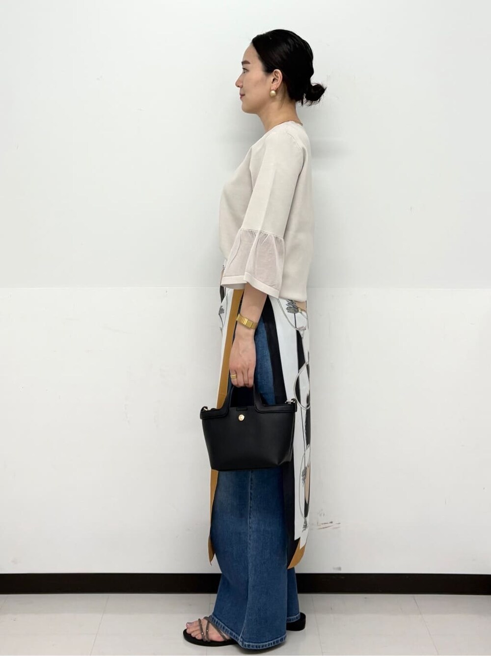 ブルー系のデニムパンツ、ブラック系のショルダーバッグ、シルバー系のサンダルを着用したレディースの春コーディネートの4枚目の写真