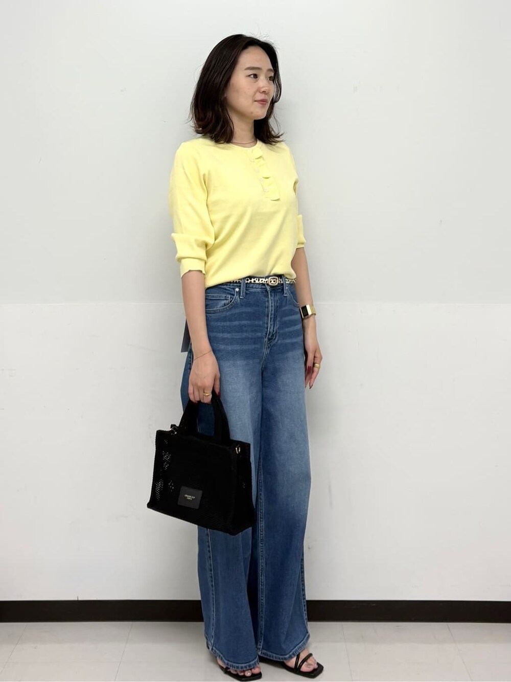 イエロー系のニット/セーター、ブルー系のデニムパンツ、ブラック系のトートバッグを着用したレディースの春コーディネートの2枚目の写真