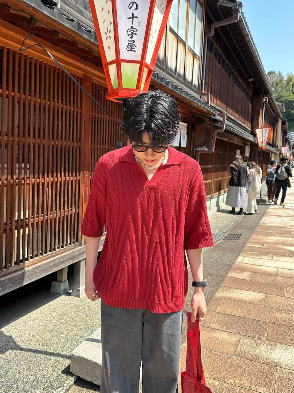 レッド系のポロシャツ、グレー系のデニムパンツ、レッド系のトートバッグを着用したメンズの夏コーディネートの2枚目の写真