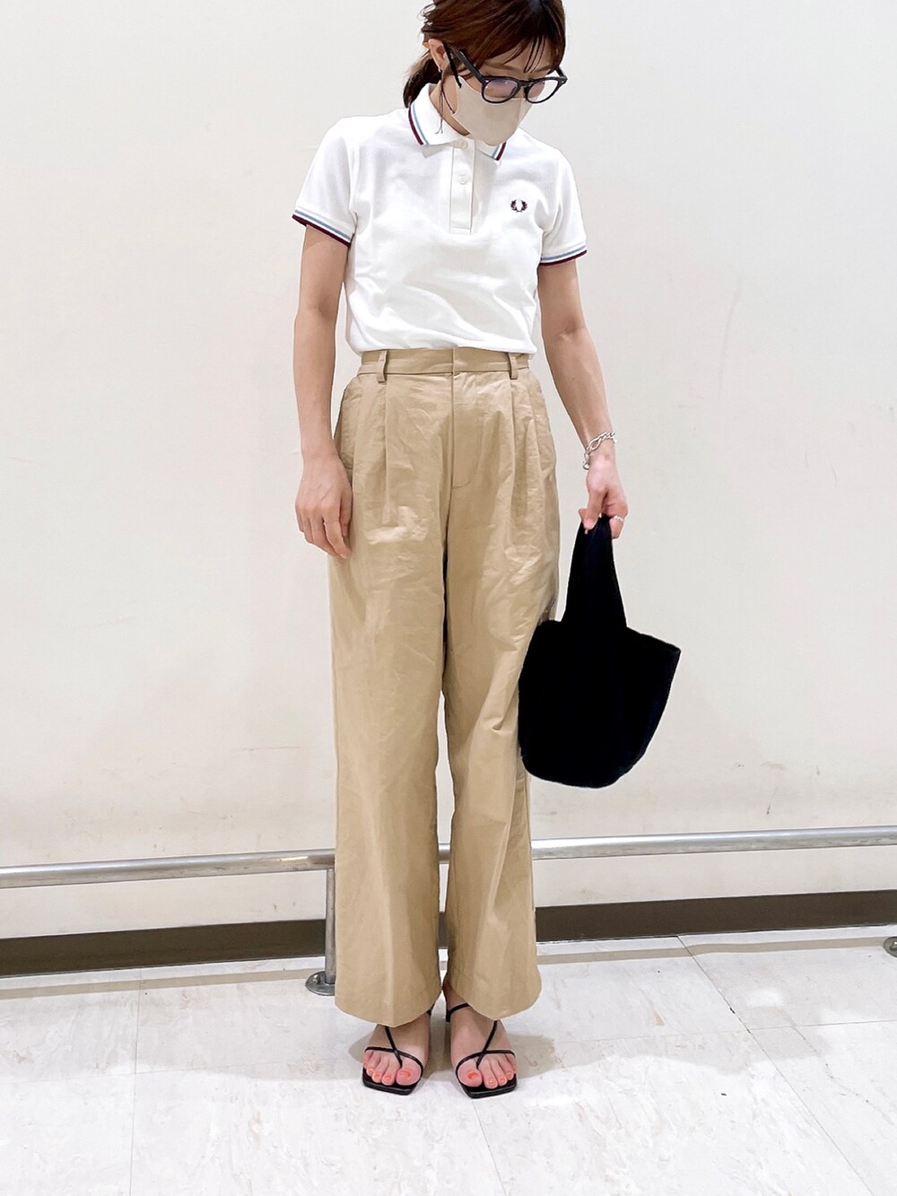 ホワイト系のポロシャツ、イエロー系のチノパンツ、ブラック系のサンダルを着用したレディースの夏コーディネートの5枚目の写真