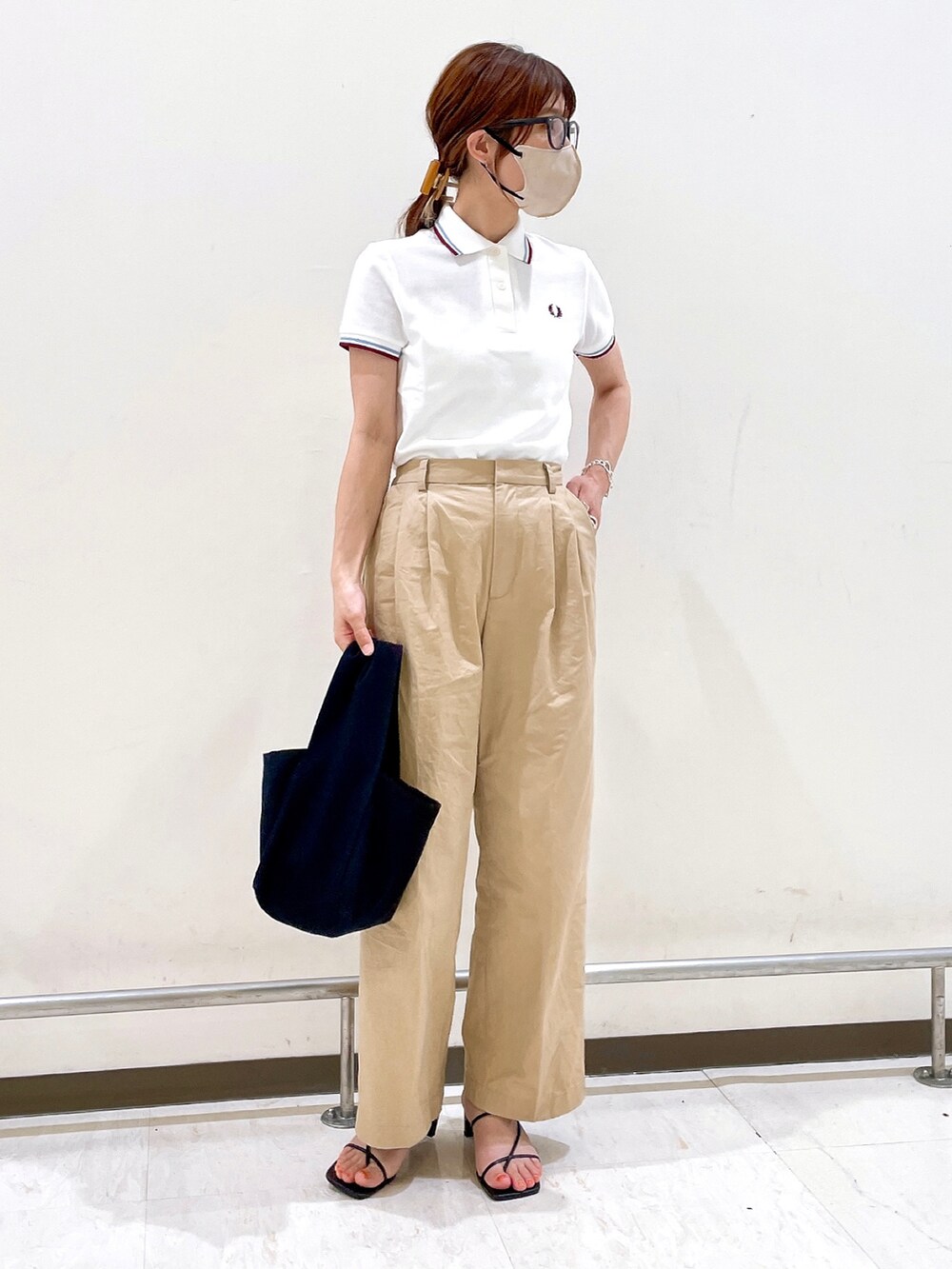ホワイト系のポロシャツ、イエロー系のチノパンツ、ブラック系のサンダルを着用したレディースの夏コーディネートの3枚目の写真