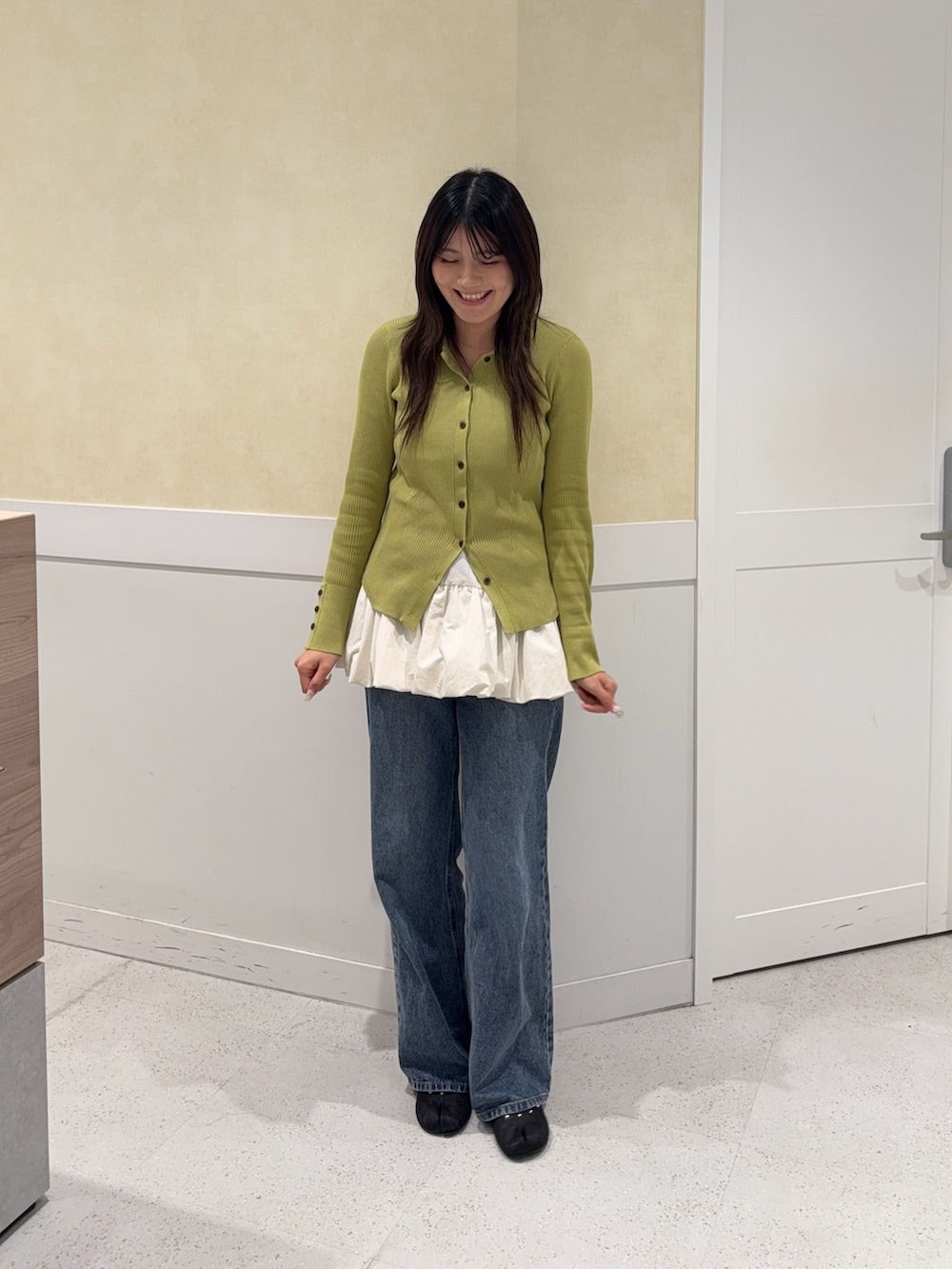グリーン系のニット/セーター、ホワイト系のキャミソール、ブルー系のデニムパンツを着用したレディースの秋コーディネートの4枚目の写真