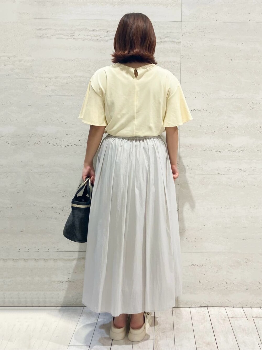 イエロー系のTシャツ/カットソー、グレー系のスカート、ブラック系のトートバッグを着用したレディースの夏コーディネートの3枚目の写真