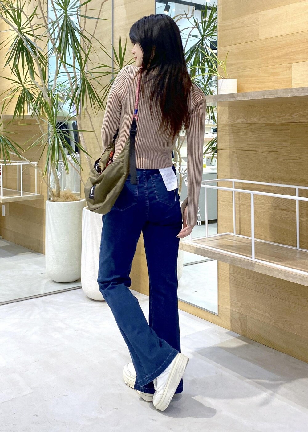 ホワイト系のスニーカー、ブルー系のデニムパンツ、グリーン系のショルダーバッグを着用したレディースの秋コーディネートの4枚目の写真
