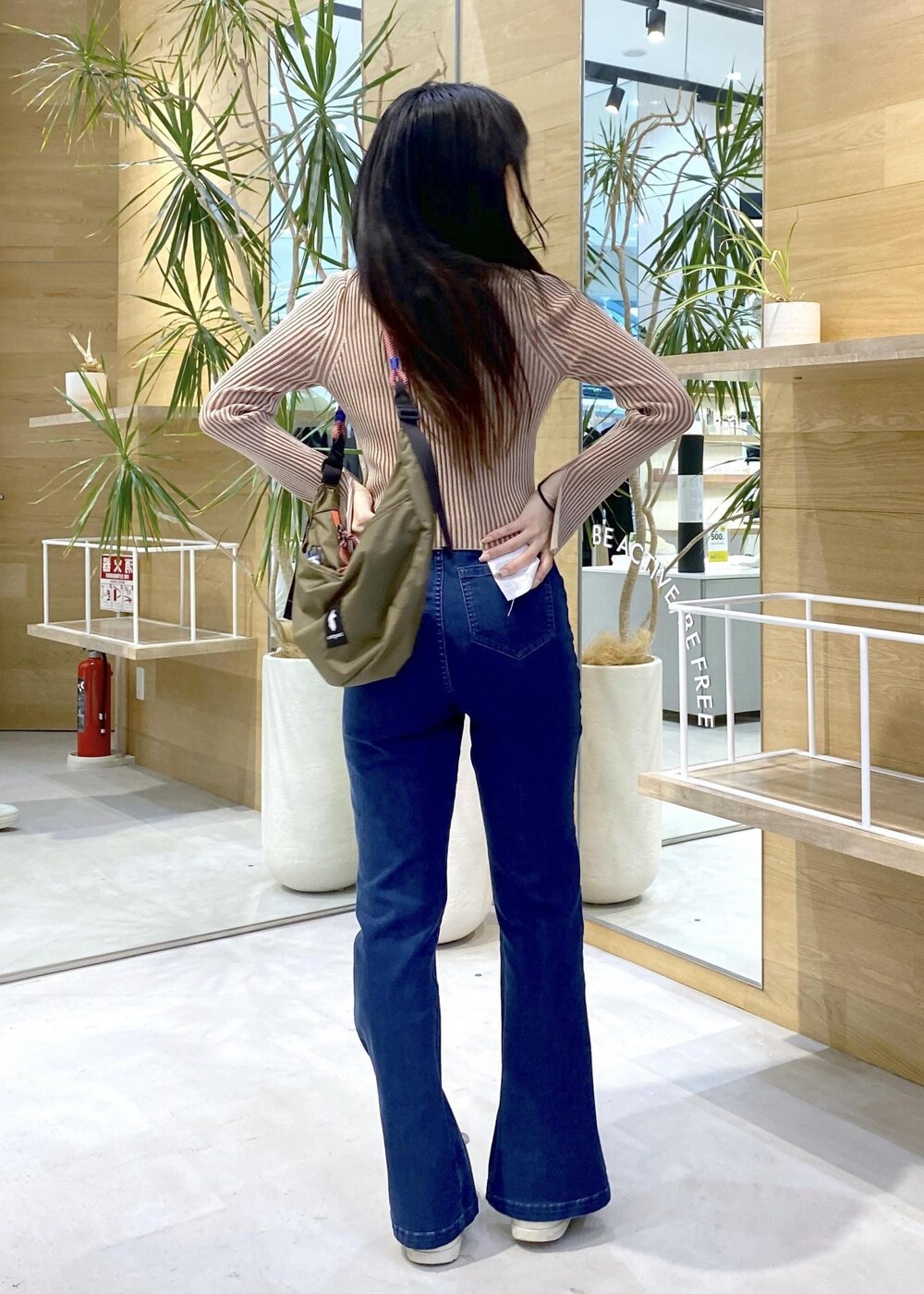 ホワイト系のスニーカー、ブルー系のデニムパンツ、グリーン系のショルダーバッグを着用したレディースの秋コーディネートの5枚目の写真