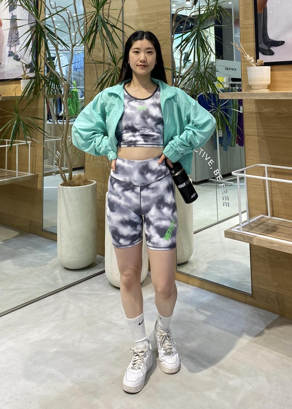 ホワイト系のスニーカー、グリーン系のナイロンジャケット、ブラック系のブラジャーを着用したレディースの春コーディネートの2枚目の写真