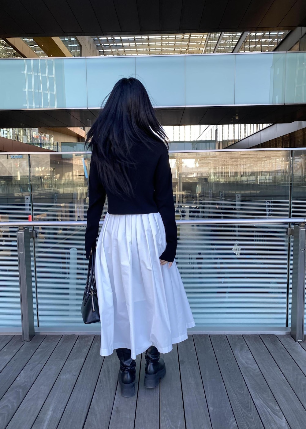 ブラック系のボストンバッグ、ブラック系のカーディガン/ボレロ、ホワイト系のスカートを着用したレディースの春コーディネートの5枚目の写真