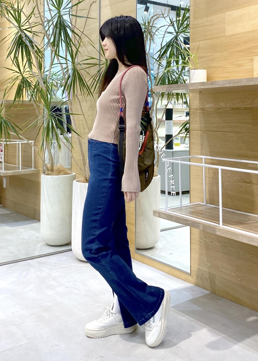 ホワイト系のスニーカー、ブルー系のデニムパンツ、グリーン系のショルダーバッグを着用したレディースの秋コーディネートの3枚目の写真