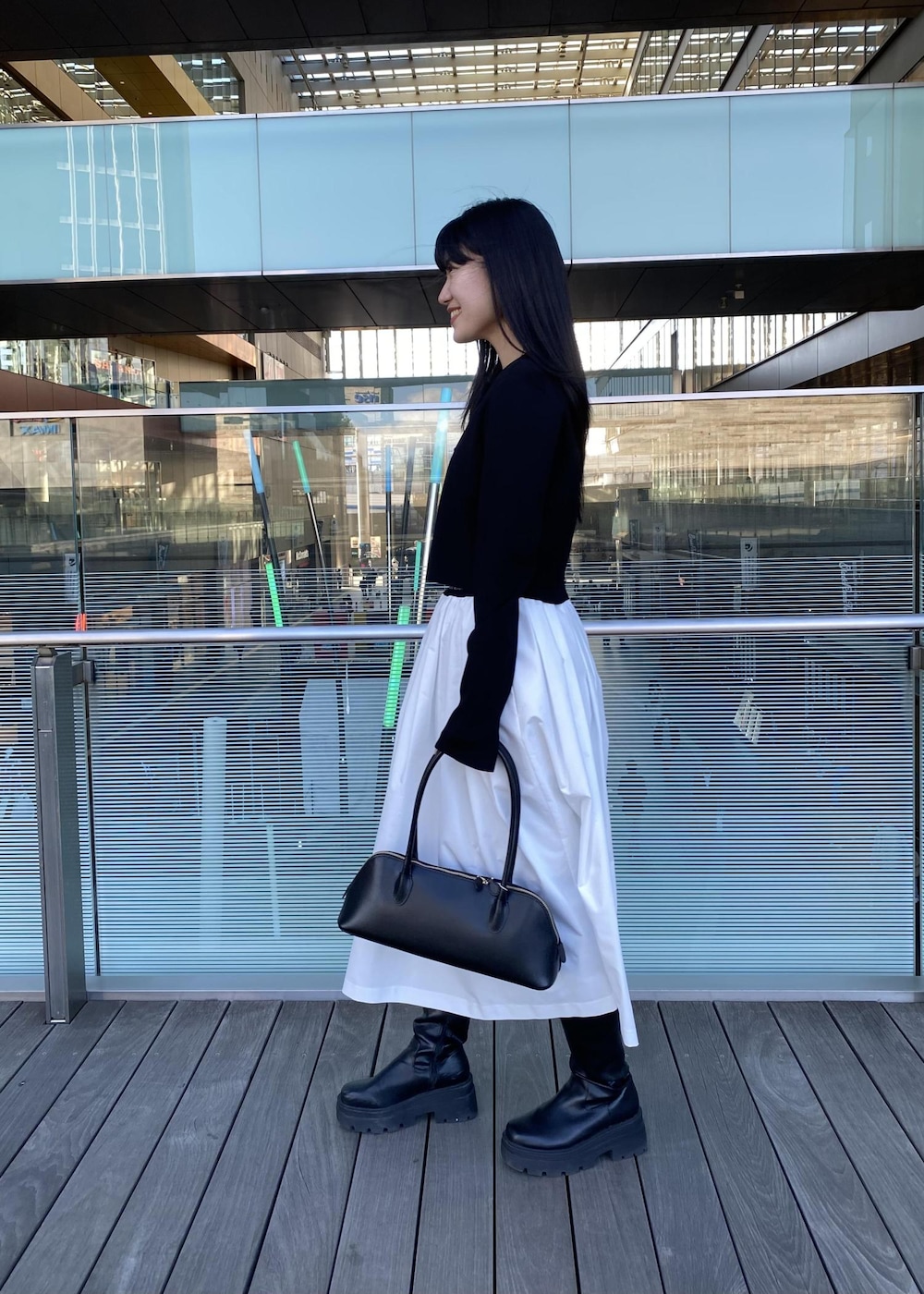 ブラック系のボストンバッグ、ブラック系のカーディガン/ボレロ、ホワイト系のスカートを着用したレディースの春コーディネートの3枚目の写真