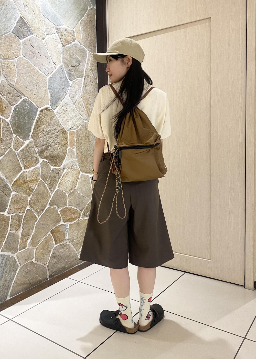 ブラウン系のバックパック/リュック、ブラウン系のその他パンツ、ベージュ系のポロシャツを着用したレディースの春コーディネートの6枚目の写真