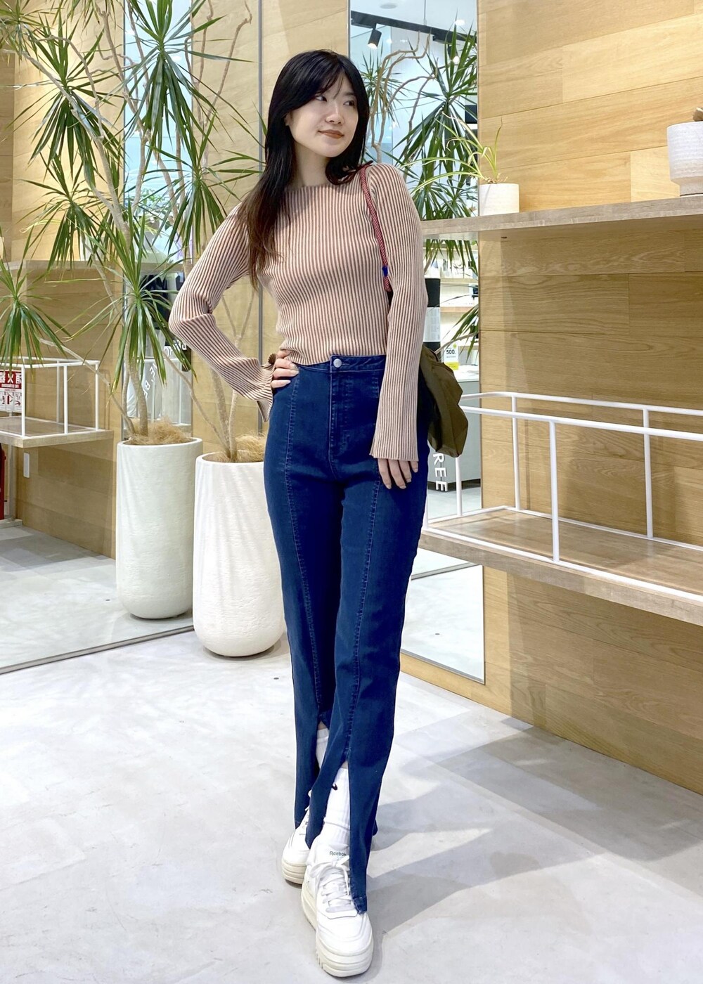 ホワイト系のスニーカー、ブルー系のデニムパンツ、グリーン系のショルダーバッグを着用したレディースの秋コーディネートの2枚目の写真