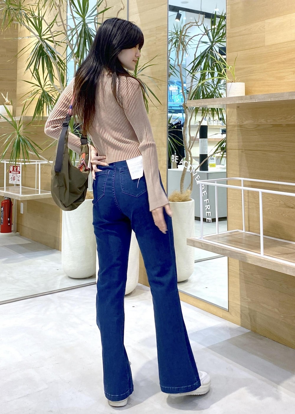 ホワイト系のスニーカー、ブルー系のデニムパンツ、グリーン系のショルダーバッグを着用したレディースの秋コーディネートの6枚目の写真