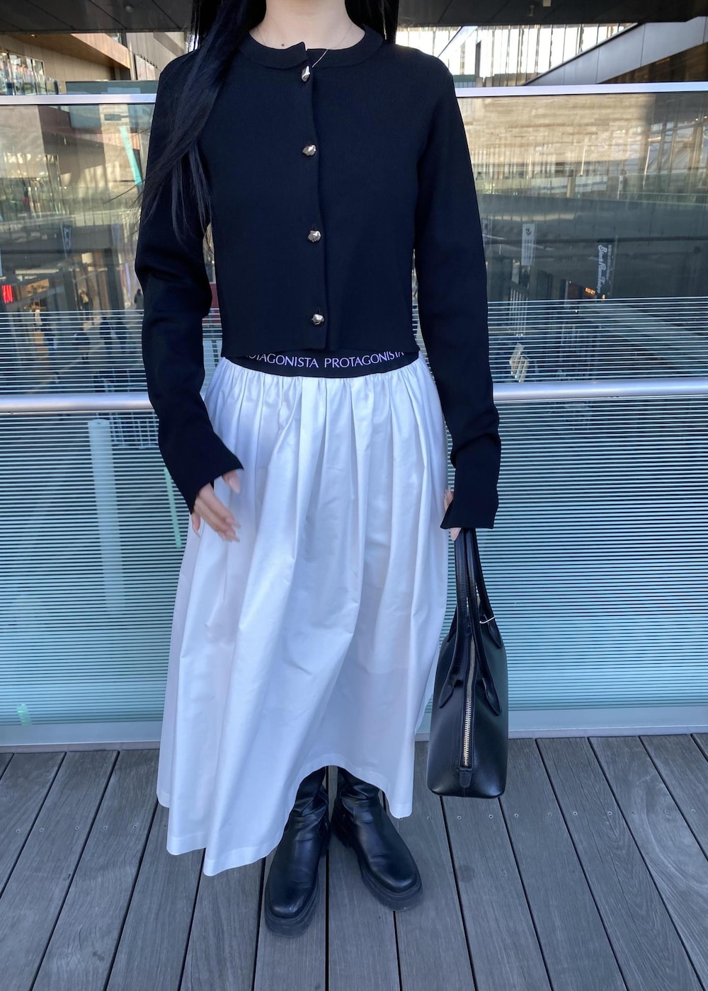 ブラック系のボストンバッグ、ブラック系のカーディガン/ボレロ、ホワイト系のスカートを着用したレディースの春コーディネートの7枚目の写真