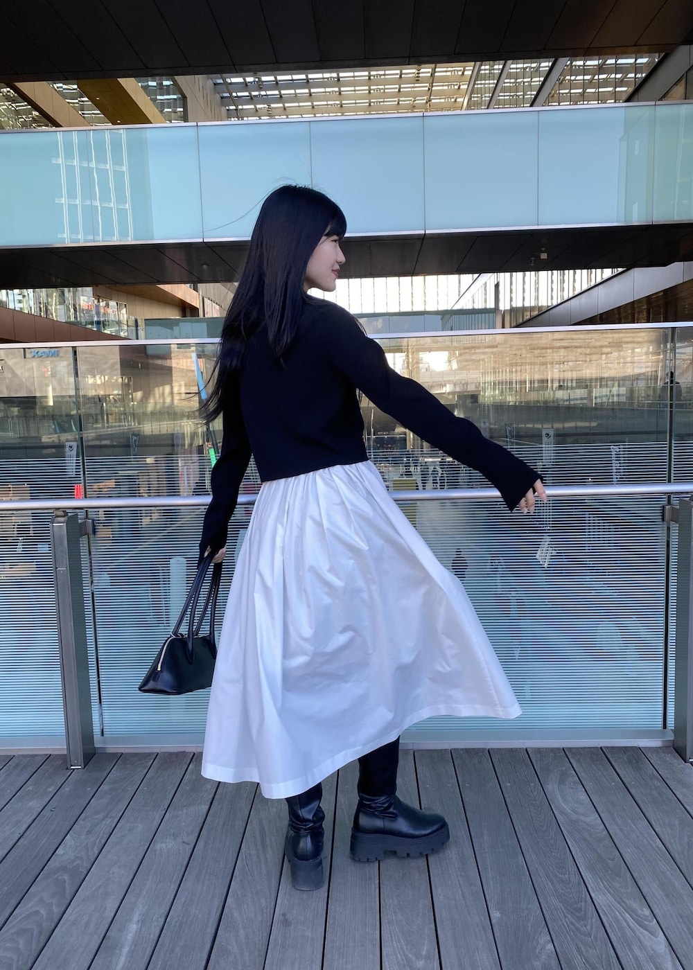 ブラック系のボストンバッグ、ブラック系のカーディガン/ボレロ、ホワイト系のスカートを着用したレディースの春コーディネートの4枚目の写真