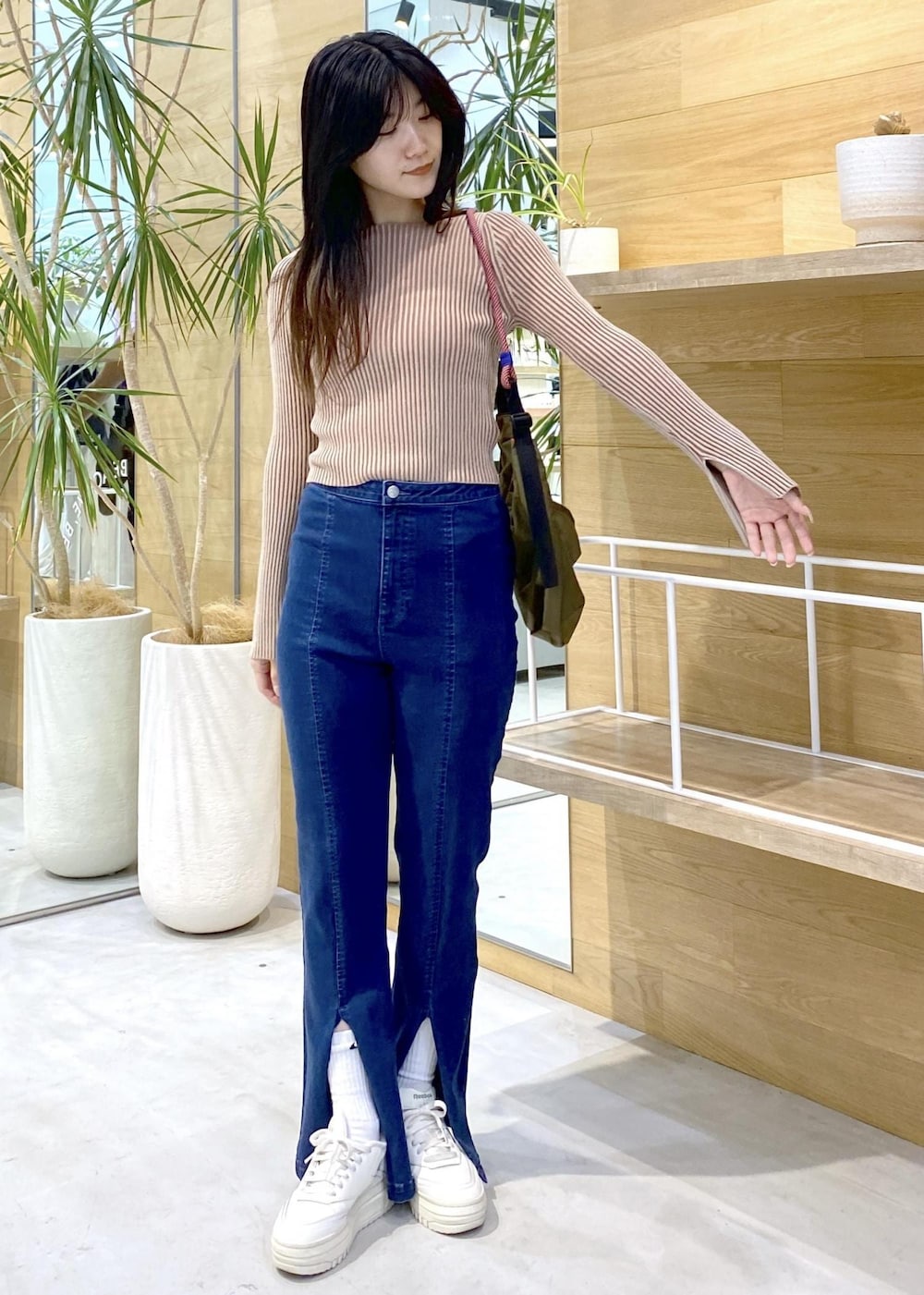 ホワイト系のスニーカー、ブルー系のデニムパンツ、グリーン系のショルダーバッグを着用したレディースの秋コーディネートの7枚目の写真