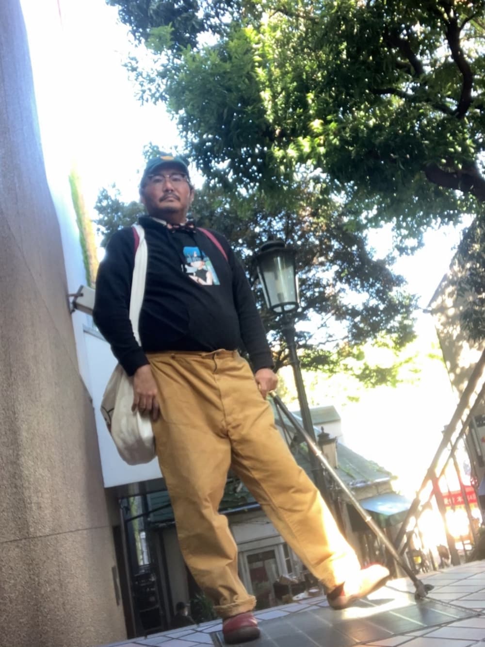 ベージュ系のショルダーバッグ、ブラウン系のスリッポン、ブルー系のキャップを着用したメンズの秋コーディネートの2枚目の写真