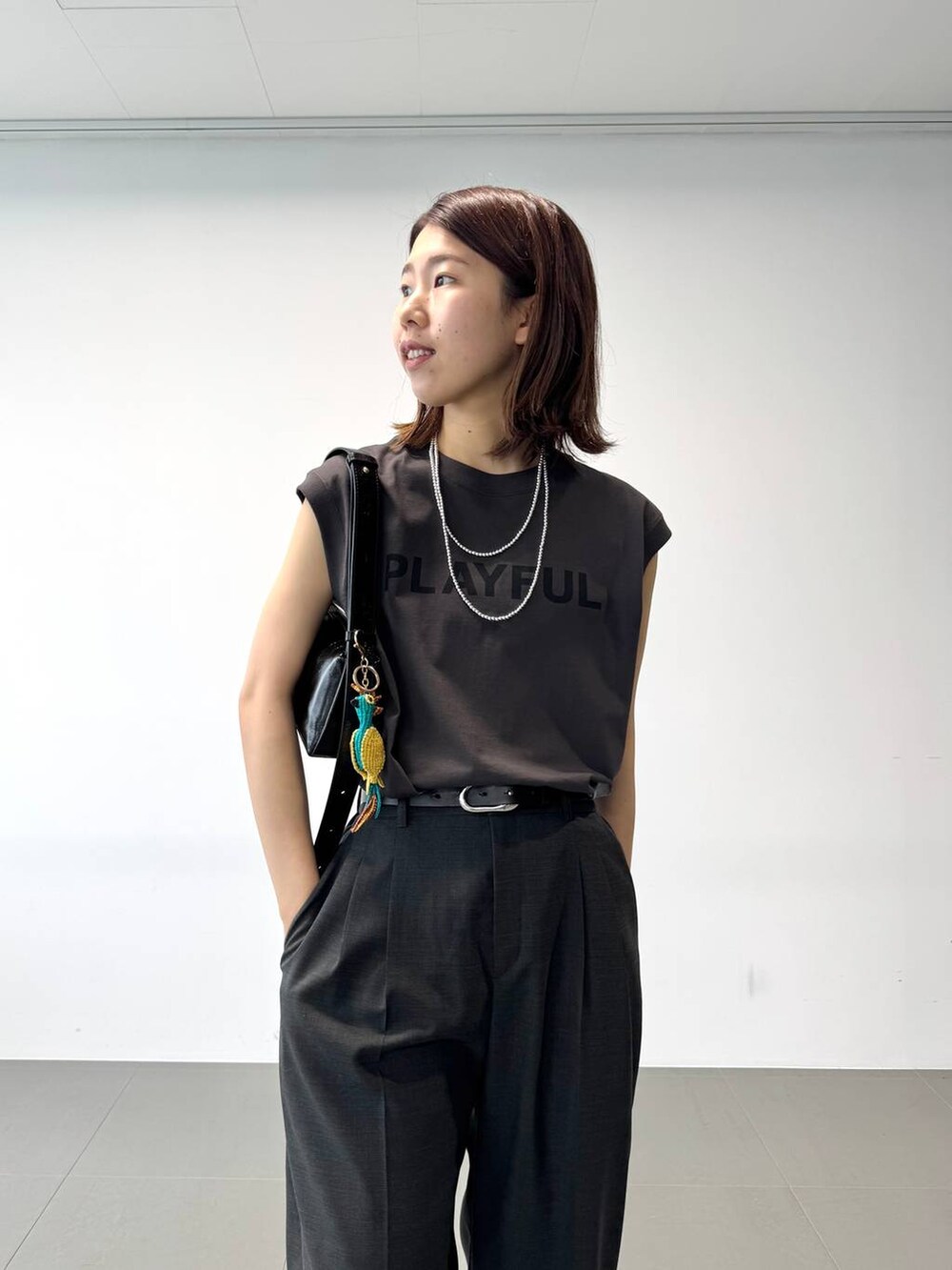 グレー系のタンクトップ、グレー系のスラックス、ブラック系のショルダーバッグを着用したレディースの夏コーディネートの7枚目の写真