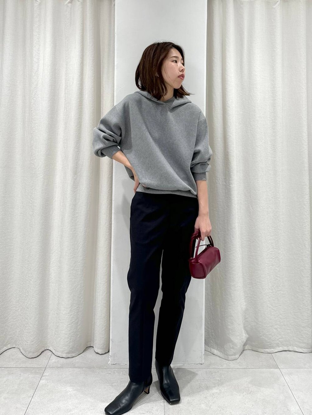レッド系のショルダーバッグ、ブラック系のスラックス、グレー系のパーカーを着用したレディースの秋コーディネートの2枚目の写真