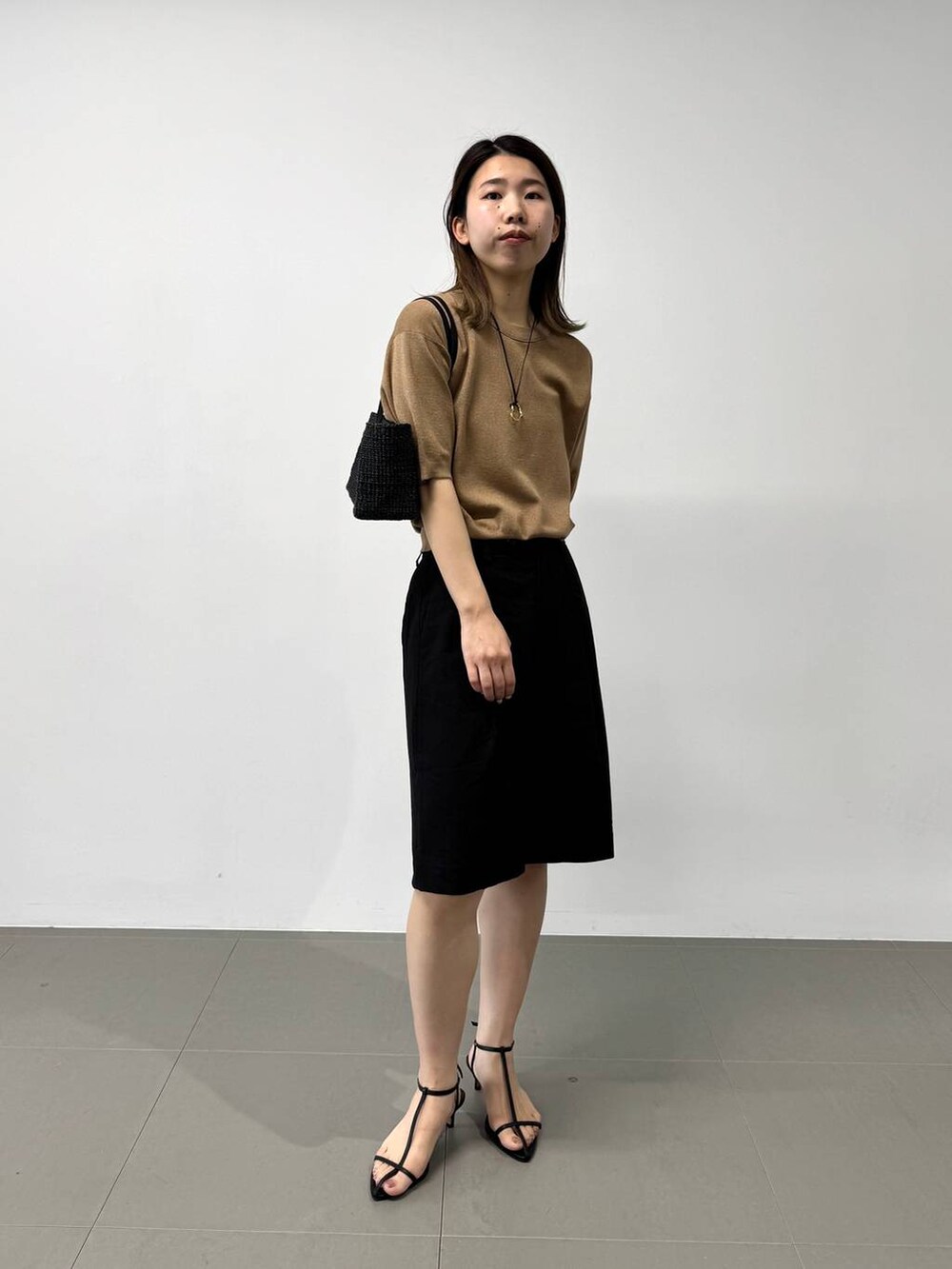 ブラック系のかごバッグ、ベージュ系のTシャツ/カットソー、ブラック系のサンダルを着用したレディースの夏コーディネートの2枚目の写真