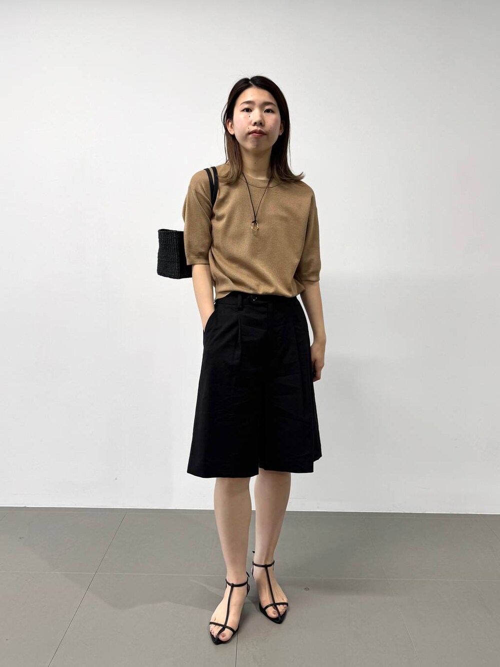 ブラック系のかごバッグ、ベージュ系のTシャツ/カットソー、ブラック系のサンダルを着用したレディースの夏コーディネートの3枚目の写真