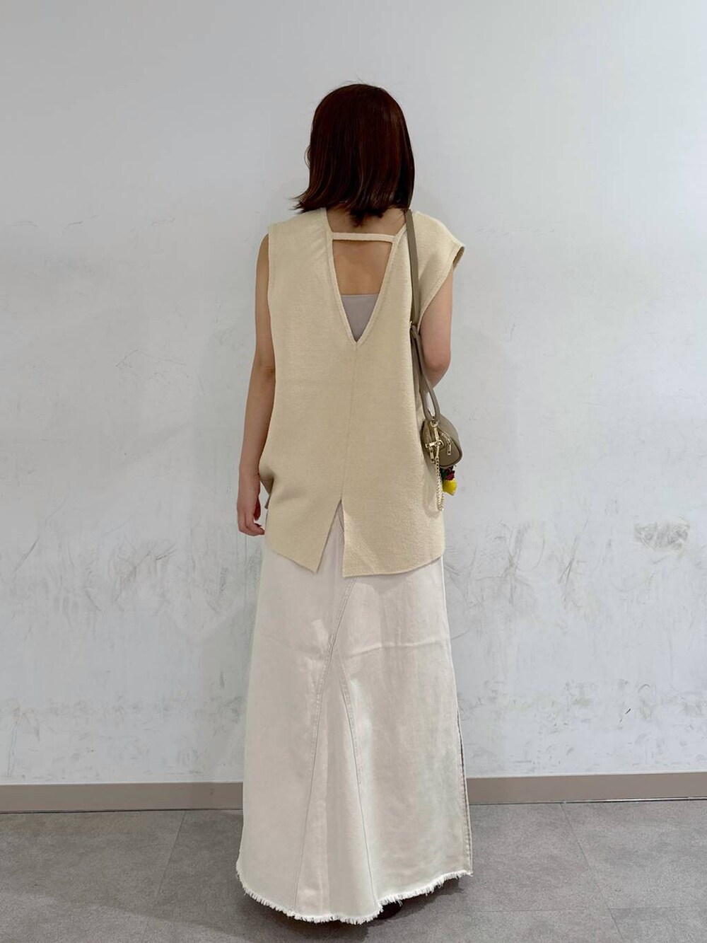 オレンジ系のキャミソール、ホワイト系のスカート、ベージュ系のベストを着用したレディースの夏コーディネートの6枚目の写真