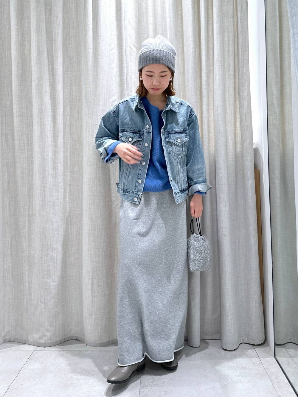ブルー系のデニムジャケット、ブルー系のニット/セーター、シルバー系のショルダーバッグを着用したレディースの秋コーディネートの2枚目の写真