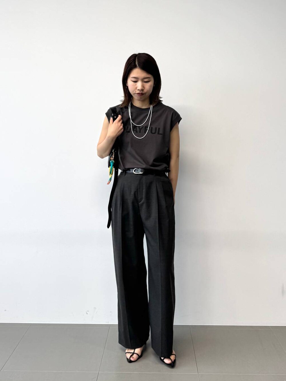 グレー系のタンクトップ、グレー系のスラックス、ブラック系のショルダーバッグを着用したレディースの夏コーディネートの2枚目の写真