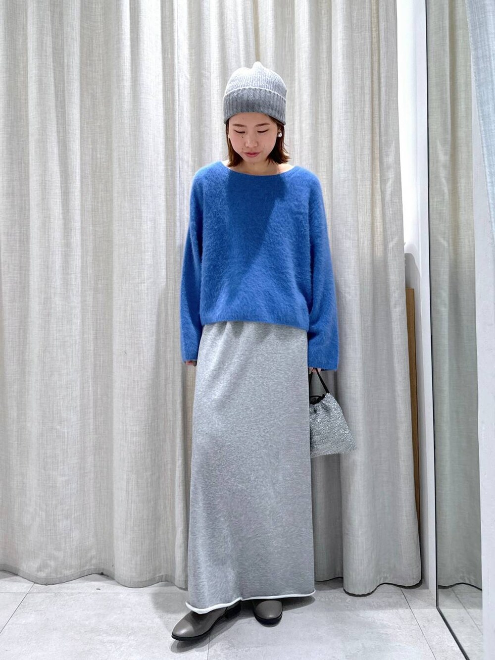 ブルー系のニット/セーター、シルバー系のショルダーバッグ、グレー系のスカートを着用したレディースの秋コーディネートの2枚目の写真