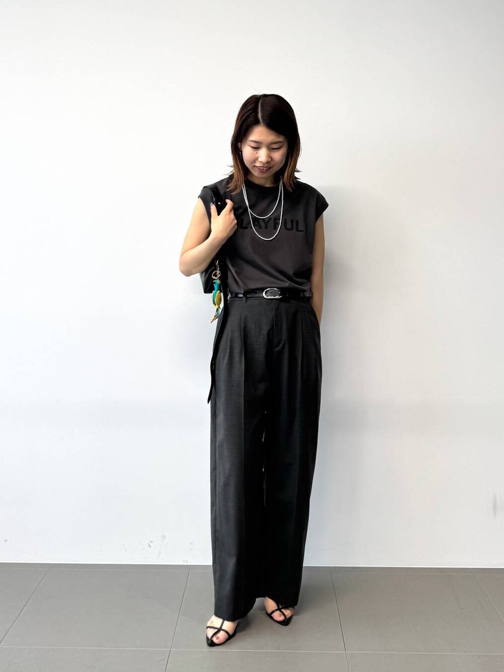 グレー系のタンクトップ、グレー系のスラックス、ブラック系のショルダーバッグを着用したレディースの夏コーディネートの3枚目の写真